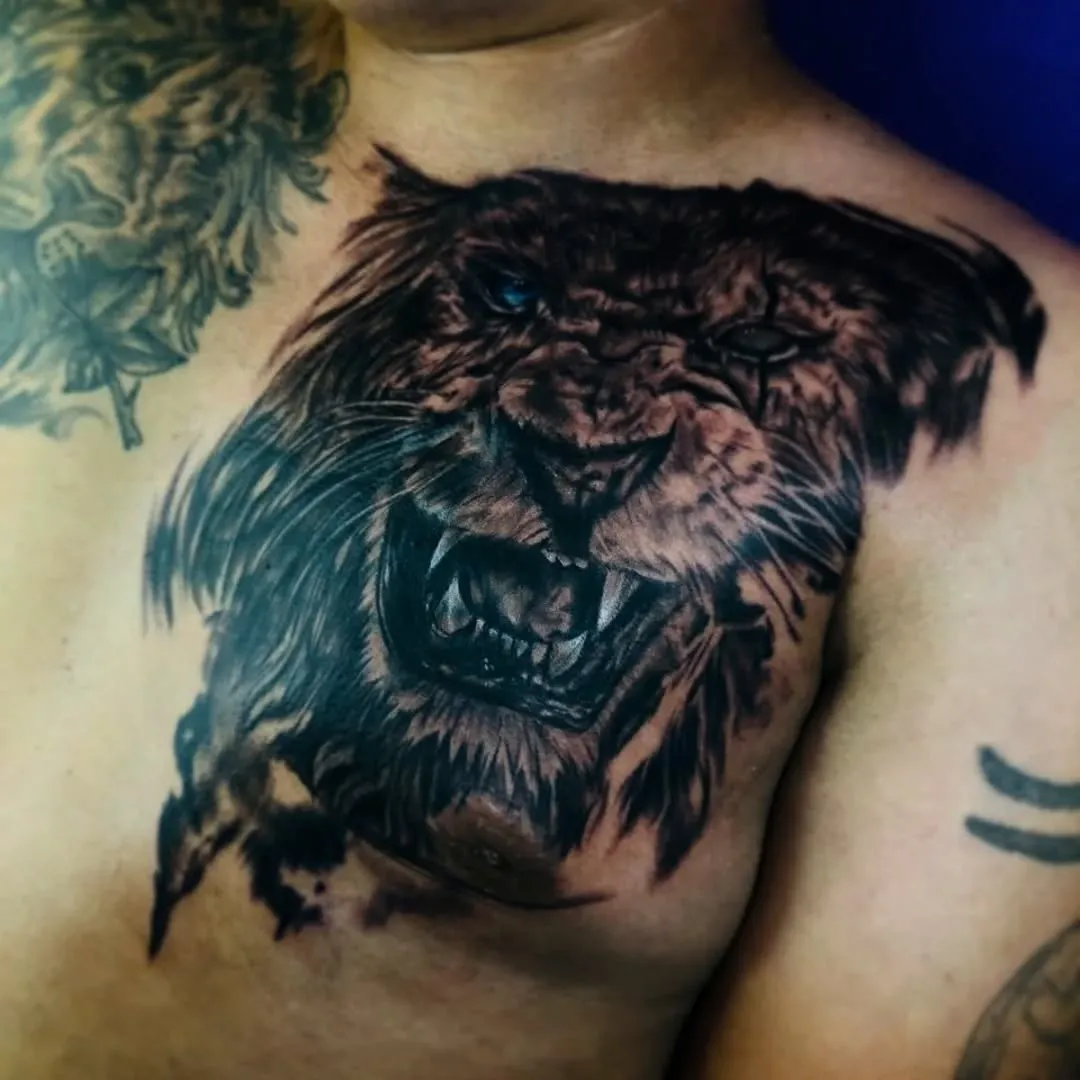 León rugiendo tatuado en el pecho con realismo en negro y gris